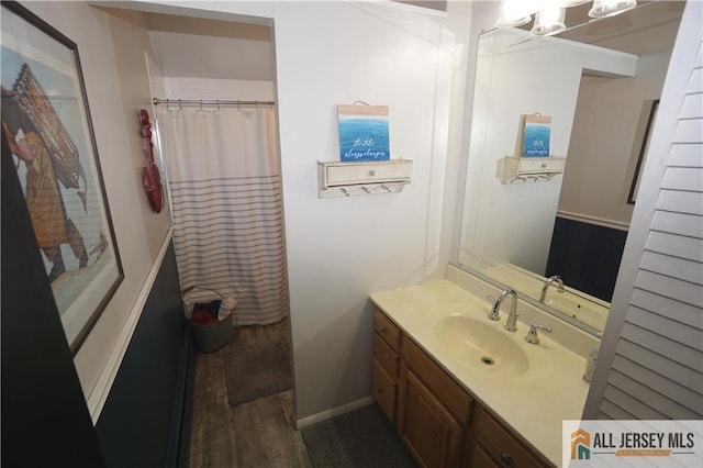 full bath with a shower with shower curtain, baseboards, wood finished floors, and vanity