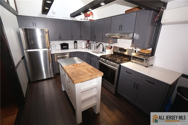 kitchen featuring dark wood-style floors, butcher block counters, stainless steel appliances, under cabinet range hood, and a sink