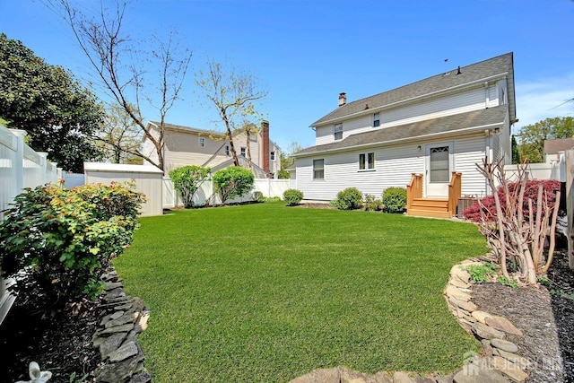 back of property featuring a fenced backyard, entry steps, a yard, and a shingled roof