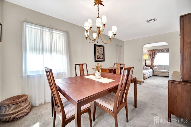 dining area with light colored carpet, arched walkways, a notable chandelier, and visible vents
