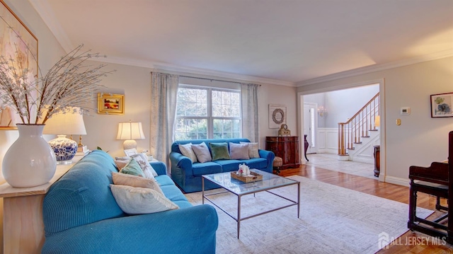 living area featuring a decorative wall, stairway, light wood-style flooring, and crown molding