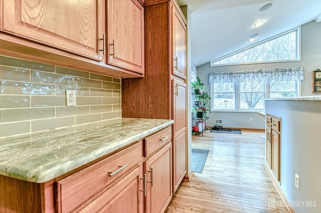 kitchen featuring visible vents, light stone countertops, light wood-type flooring, lofted ceiling, and decorative backsplash