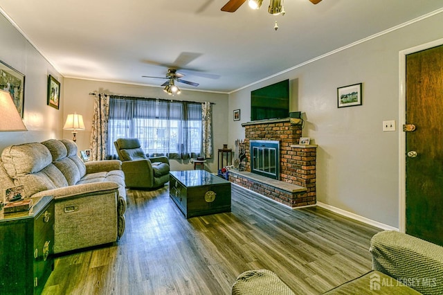 living area with wood finished floors, baseboards, ceiling fan, crown molding, and a brick fireplace