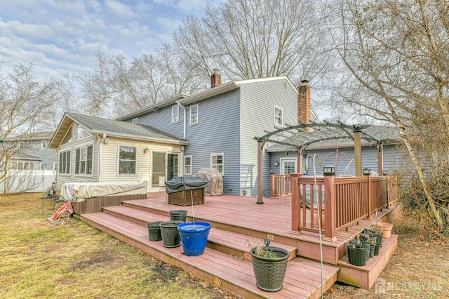 rear view of house with a deck, a covered hot tub, a pergola, and a chimney