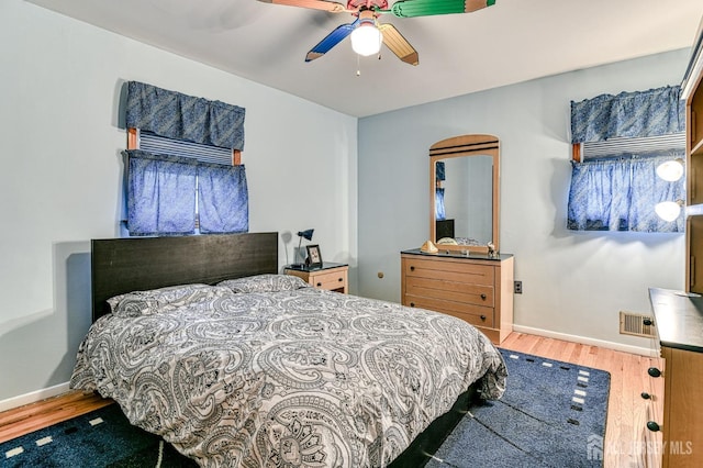 bedroom featuring ceiling fan, visible vents, baseboards, and wood finished floors