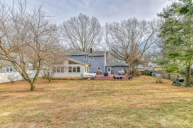 rear view of property featuring a chimney, a wooden deck, a yard, and fence