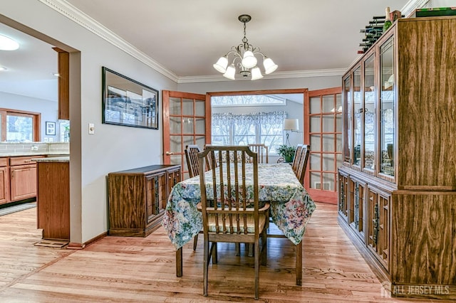 dining area with baseboards, light wood-type flooring, an inviting chandelier, and ornamental molding