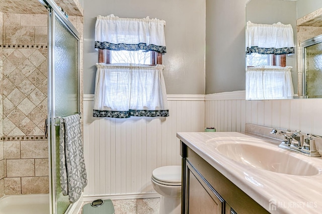 full bath featuring vanity, toilet, a stall shower, and wainscoting