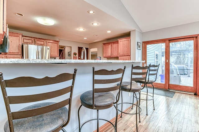 kitchen with a kitchen bar, brown cabinets, freestanding refrigerator, recessed lighting, and light wood finished floors