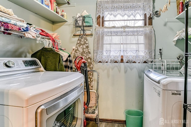 clothes washing area featuring washing machine and clothes dryer, laundry area, and wood finished floors