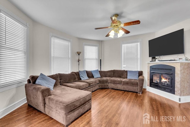 living room featuring a glass covered fireplace, baseboards, a ceiling fan, and wood finished floors