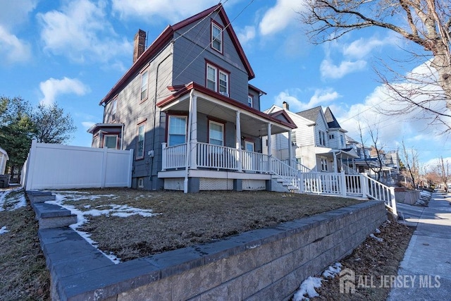 view of side of property featuring covered porch, a chimney, and fence