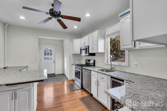 kitchen featuring light stone counters, a sink, wine cooler, appliances with stainless steel finishes, and white cabinetry