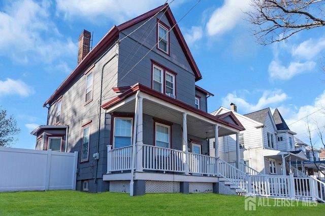 view of front of house with a front yard, fence, covered porch, and a chimney