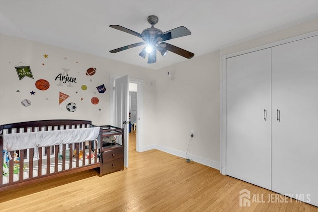 bedroom featuring a crib, wood finished floors, baseboards, and a closet