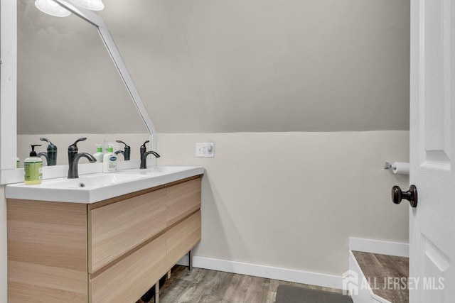 bathroom with baseboards, vaulted ceiling, double vanity, wood finished floors, and a sink