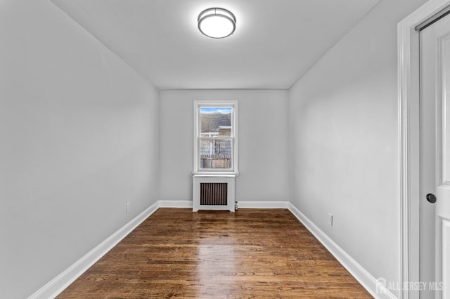 unfurnished room with dark wood-type flooring, radiator, and baseboards