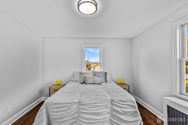 bedroom featuring multiple windows, radiator, dark wood-type flooring, and baseboards