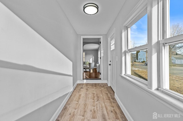 hallway with light wood finished floors, a healthy amount of sunlight, and baseboards