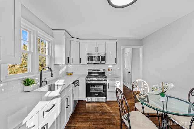 kitchen with a sink, backsplash, dark wood finished floors, white cabinetry, and appliances with stainless steel finishes