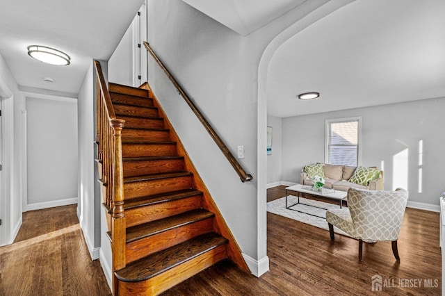 stairs featuring wood finished floors, baseboards, and arched walkways