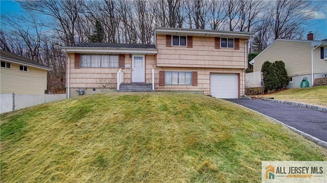 split level home with aphalt driveway, a front yard, fence, and an attached garage