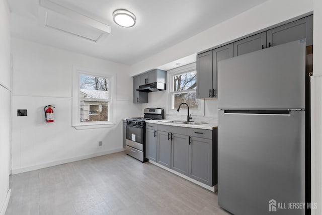 kitchen with under cabinet range hood, a sink, gray cabinets, freestanding refrigerator, and range with gas cooktop