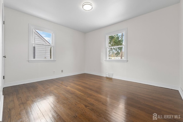 empty room with baseboards, visible vents, and dark wood-type flooring