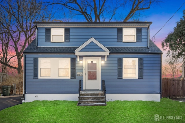 view of front of home with entry steps, a shingled roof, fence, and a front yard