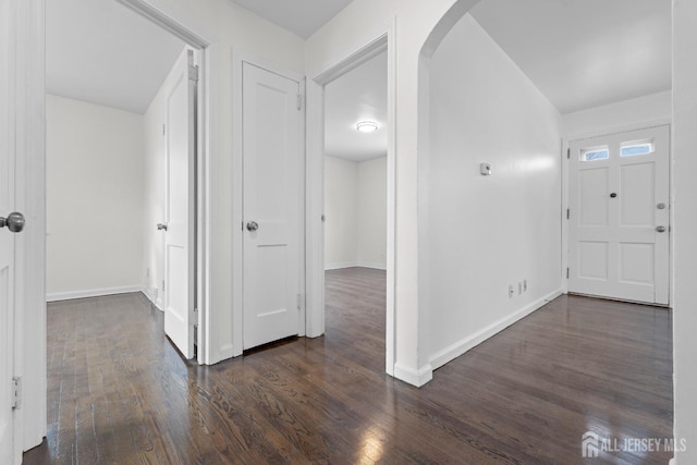 entryway with arched walkways, dark wood-style flooring, and baseboards