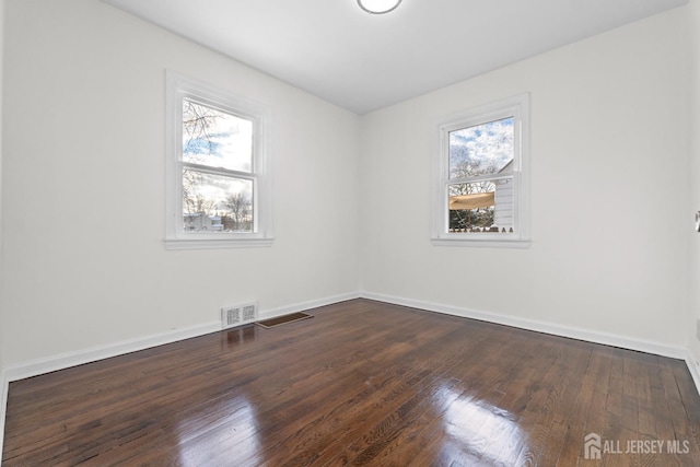 empty room with baseboards, visible vents, dark wood-style flooring, and a wealth of natural light