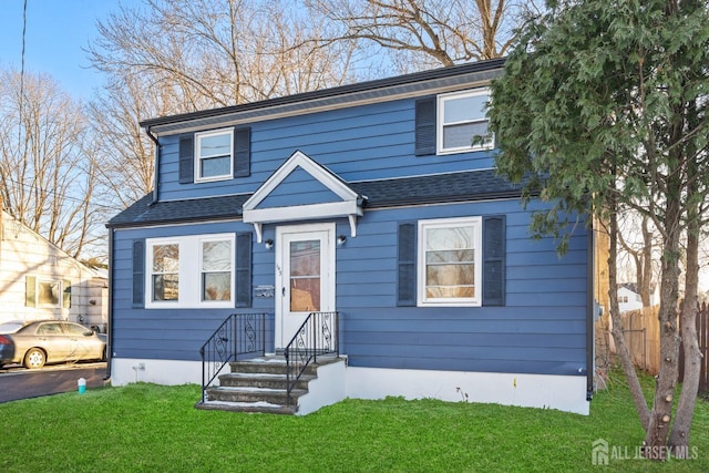 view of front facade with roof with shingles, a front yard, and fence