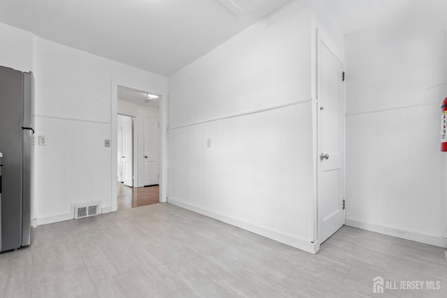 unfurnished bedroom featuring a wainscoted wall, visible vents, and freestanding refrigerator