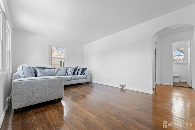 living room featuring dark wood-style floors, visible vents, arched walkways, and baseboards