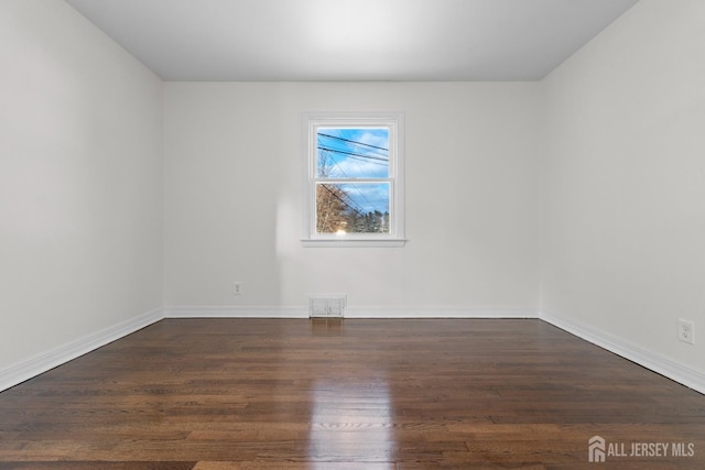 unfurnished room with baseboards, visible vents, and dark wood-style flooring