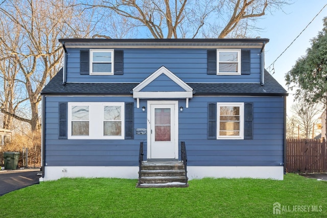 view of front facade featuring entry steps, a shingled roof, a front yard, and fence