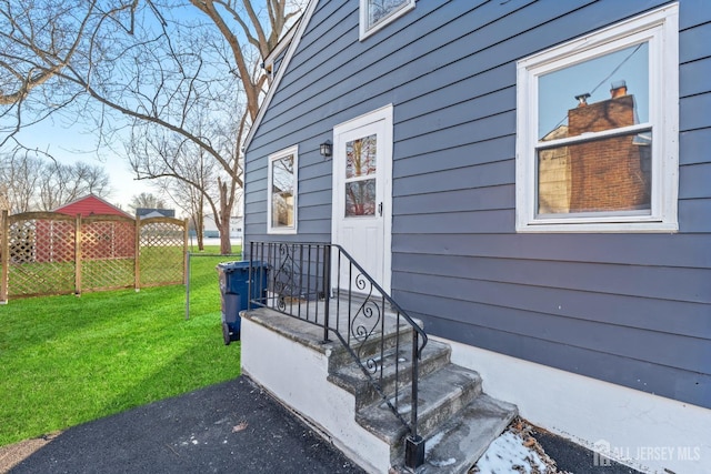 doorway to property with fence and a lawn