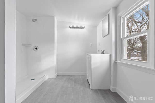 bathroom with baseboards, wood finished floors, tiled shower, and vanity