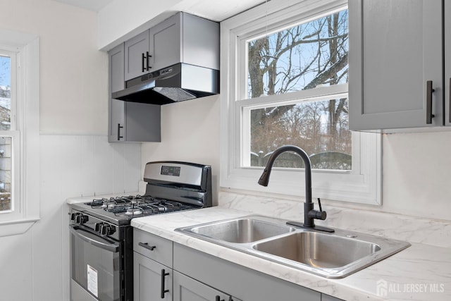 kitchen featuring plenty of natural light, range with gas cooktop, gray cabinets, under cabinet range hood, and a sink