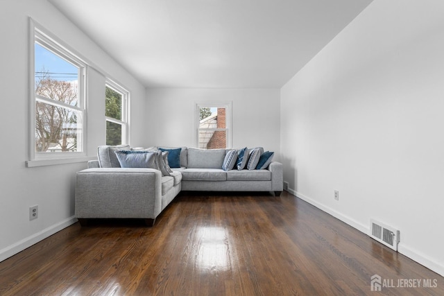 living room with dark wood-style flooring, visible vents, and baseboards