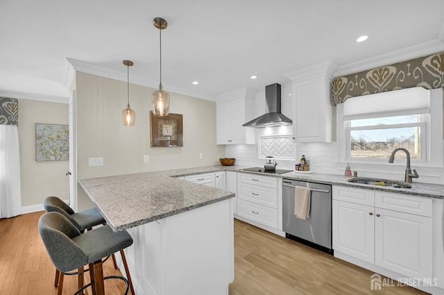 kitchen with a peninsula, a sink, white cabinets, stainless steel dishwasher, and wall chimney exhaust hood