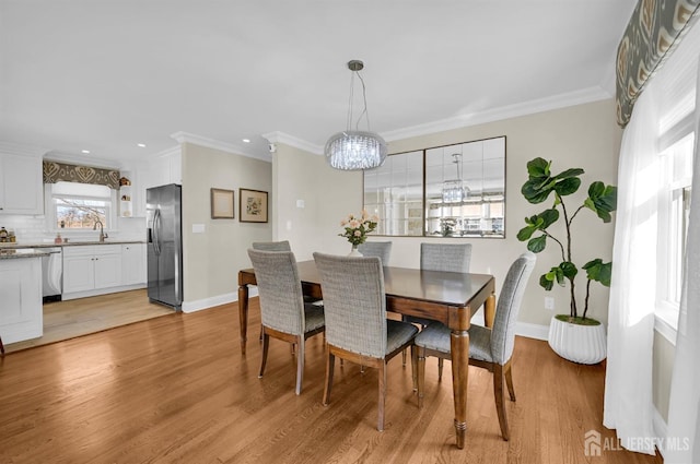 dining area with baseboards, ornamental molding, a notable chandelier, and light wood-style floors