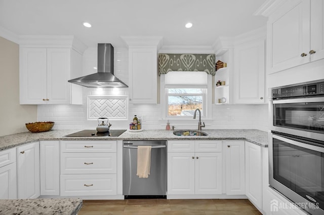 kitchen with light stone counters, a sink, white cabinets, wall chimney range hood, and appliances with stainless steel finishes