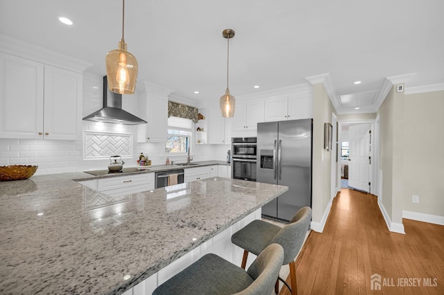 kitchen featuring white cabinets, appliances with stainless steel finishes, hanging light fixtures, light stone countertops, and wall chimney range hood