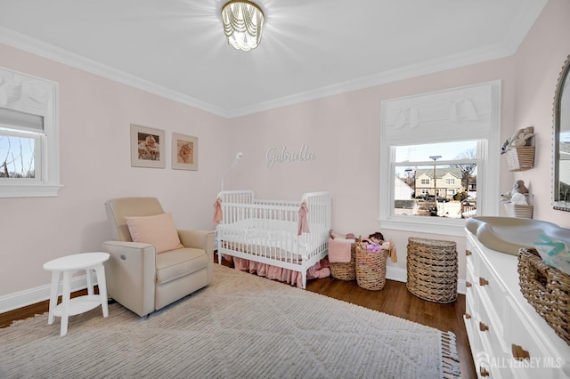 bedroom featuring a nursery area, crown molding, baseboards, and wood finished floors