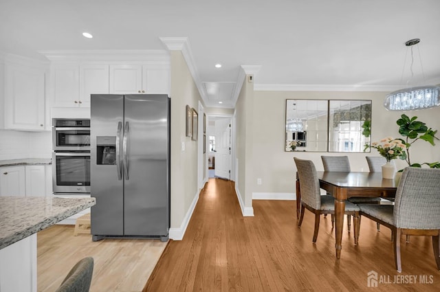 kitchen featuring pendant lighting, appliances with stainless steel finishes, ornamental molding, white cabinets, and light stone countertops