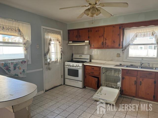 kitchen featuring backsplash, white gas range, light countertops, under cabinet range hood, and a sink