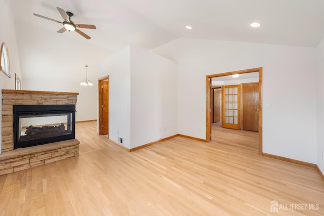 unfurnished living room featuring vaulted ceiling, ceiling fan with notable chandelier, a fireplace, and light hardwood / wood-style flooring