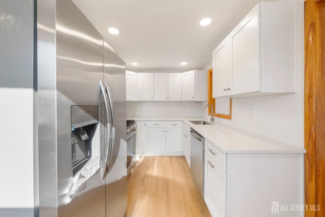 kitchen featuring stainless steel appliances, white cabinetry, sink, and light wood-type flooring