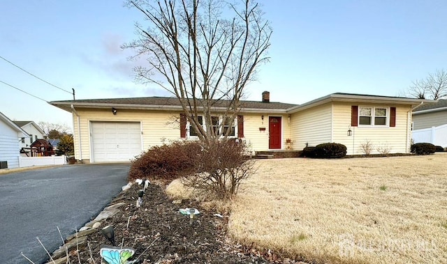 ranch-style home featuring aphalt driveway, an attached garage, a chimney, and a front yard